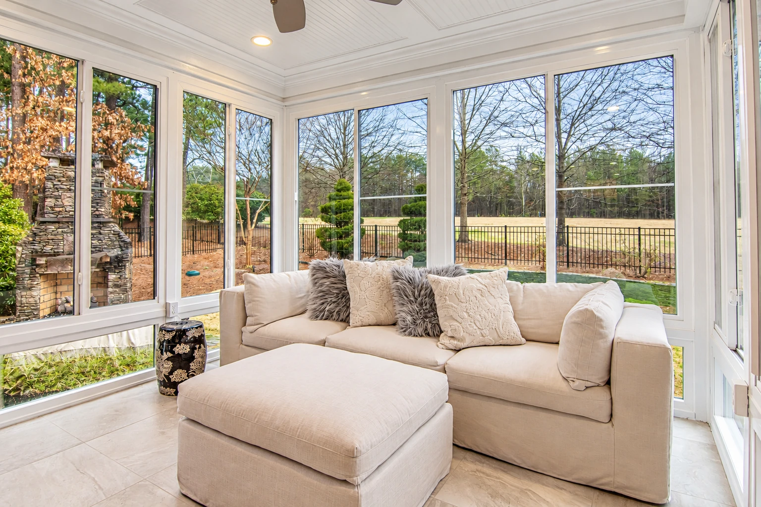 Bright all-season sunroom with large white-framed windows, a beige sectional sofa, and views of the yard.