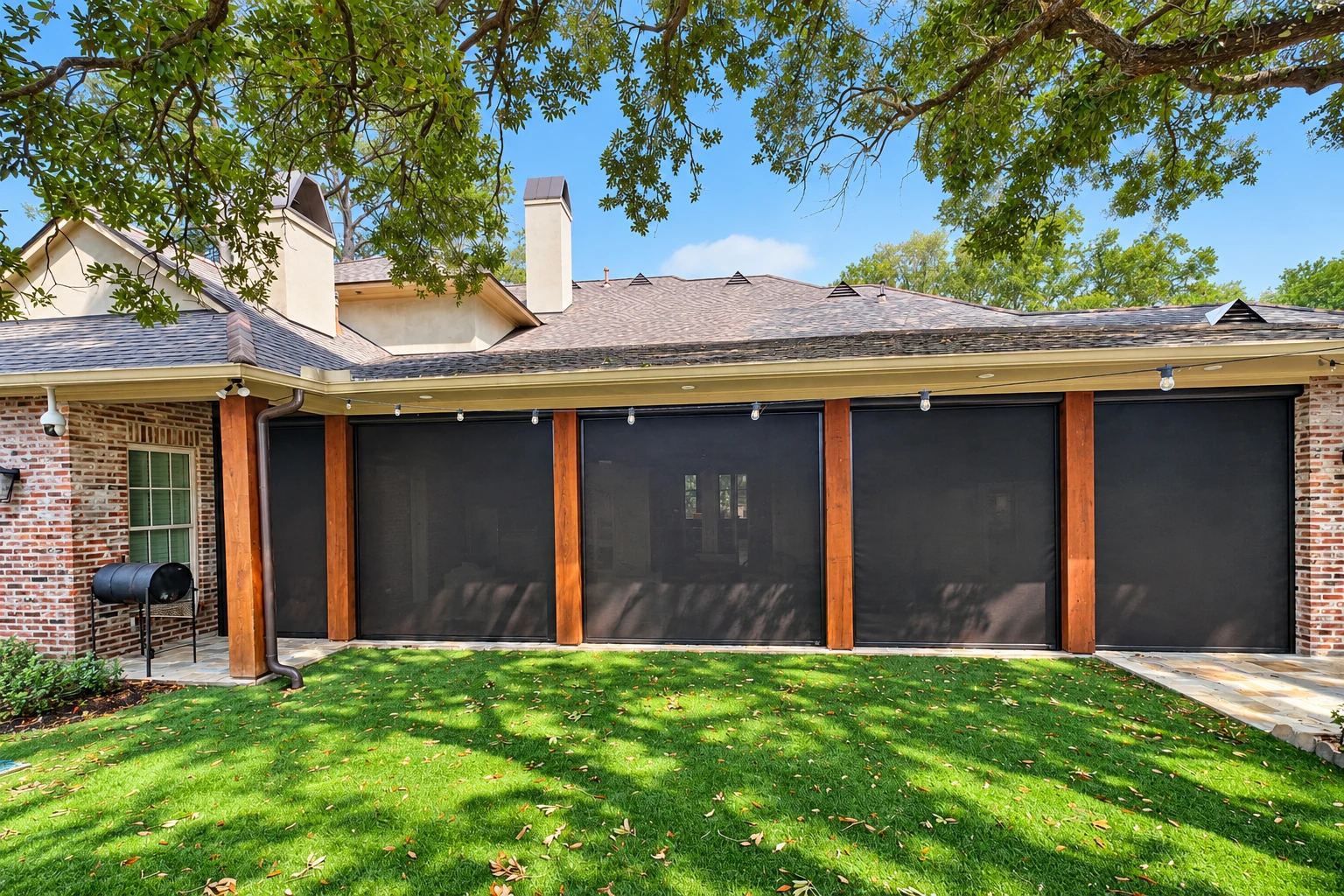 Enclosed patio with dark mesh screens between wooden posts, beside a brick house and green lawn.
