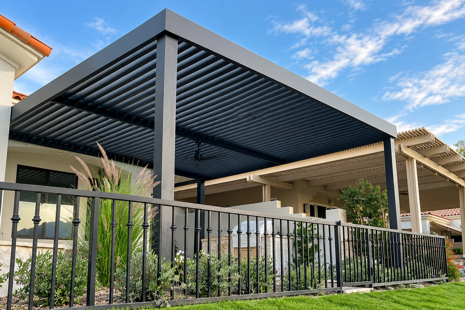Modern dark metal patio cover with a slatted roof shading a fenced outdoor patio.